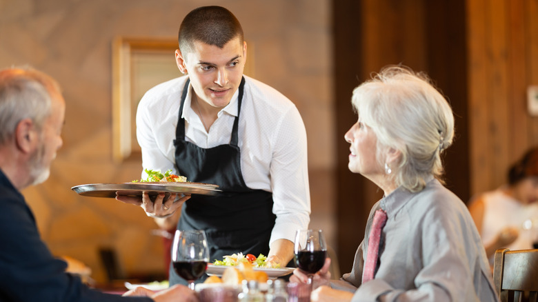 Young server at table with senior couple