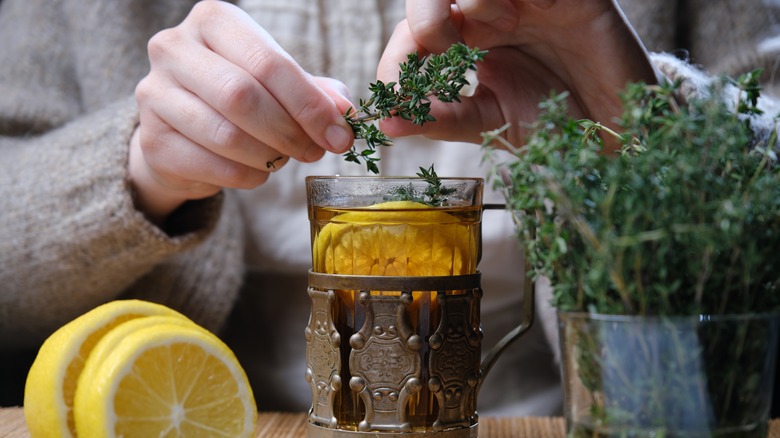 Closeup of someone adding thyme to cup of tea with lemon.