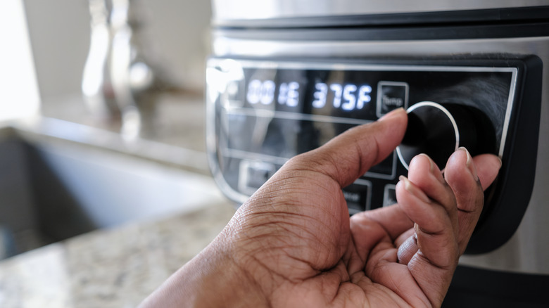 A hand adjusting the knob on an air fryer