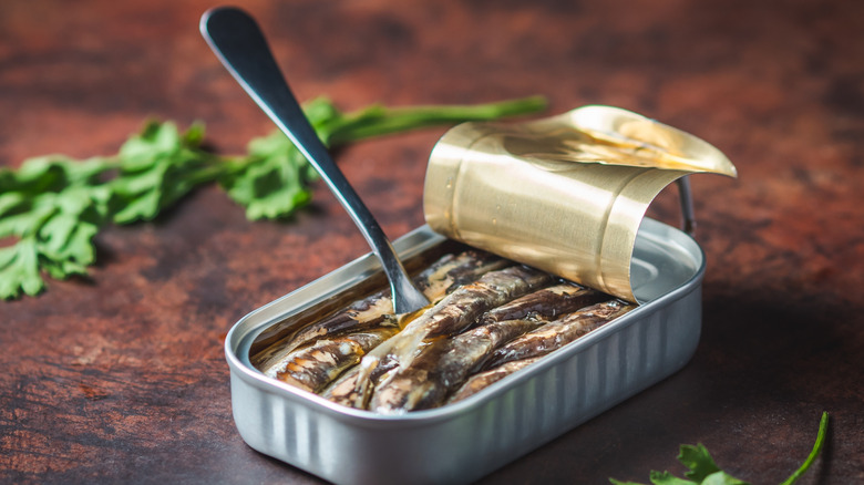 A fork in a can of sardines on a dark wooden table