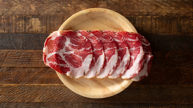 Slices of capicola on yellow plate, overhead view