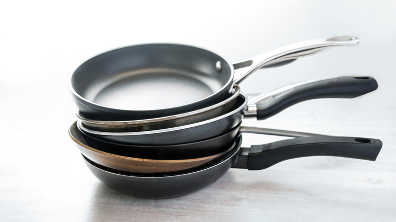 Stack of frying pans made from cast iron, carbon steel, non-stick coated and stainless steel