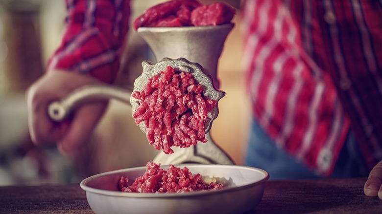 a person in plaid cranks a meat grinder for ground meat