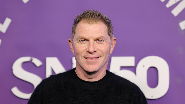 Bobby Flay smiling in front of purple backdrop.
