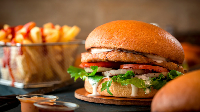 Close-up of chicken burger with several fillings and a basket of fries.