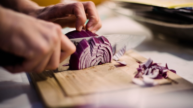 hands chop red onion with a knife