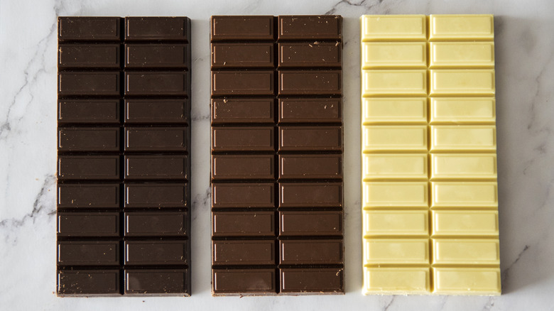 Dark, milk, and white chocolate bars on marble surface, closeup.