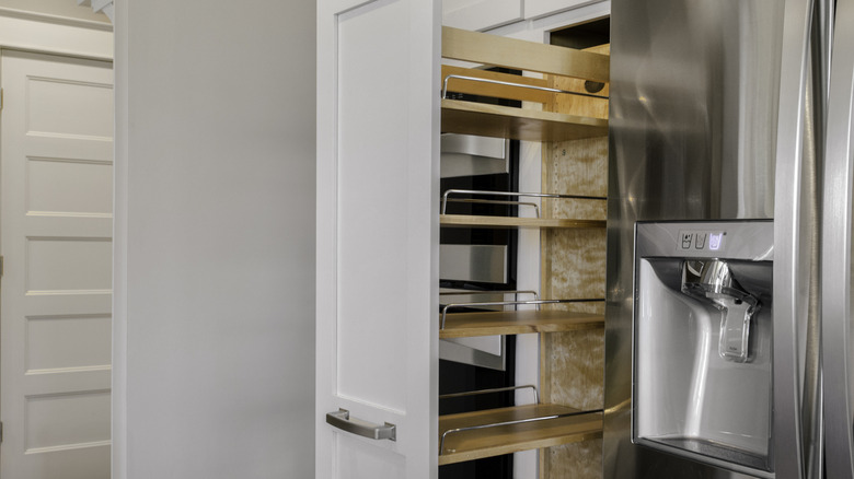 A set of pull-out shelves in a pantry next to a stainless steel fridge