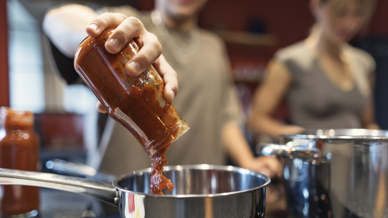 Someone pouring a jar of tomato sauce into a pan