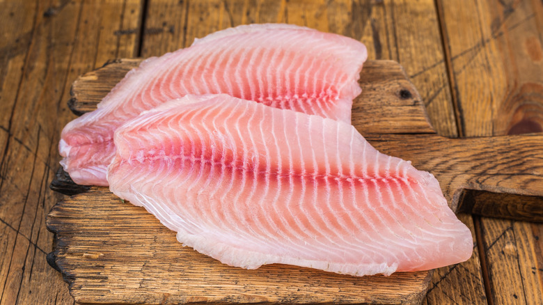 Raw tilapia fish fillets on a wooden cutting board