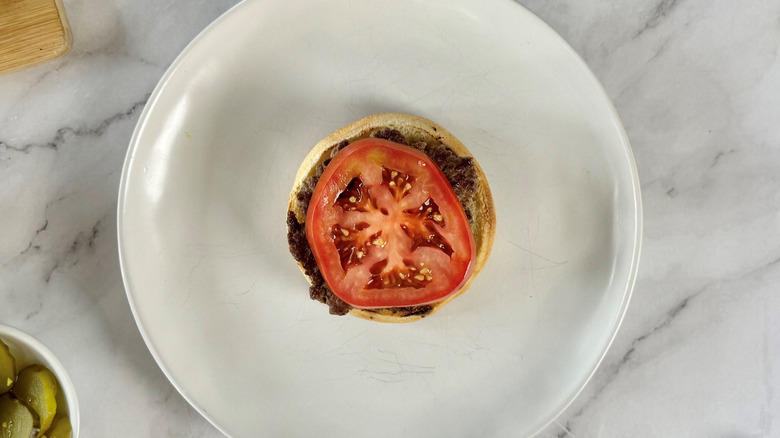 burger patty and tomato on a bun on a white plate