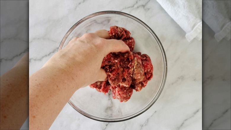 hand squishing ground meat in a clear bowl