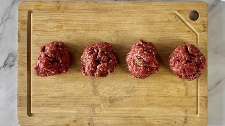 balls of ground meat laid out in a row on a wooden cutting board