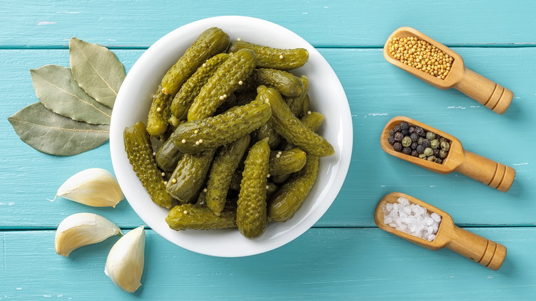 Bowl of cornichons next to garlic, bay leaves, and spices.