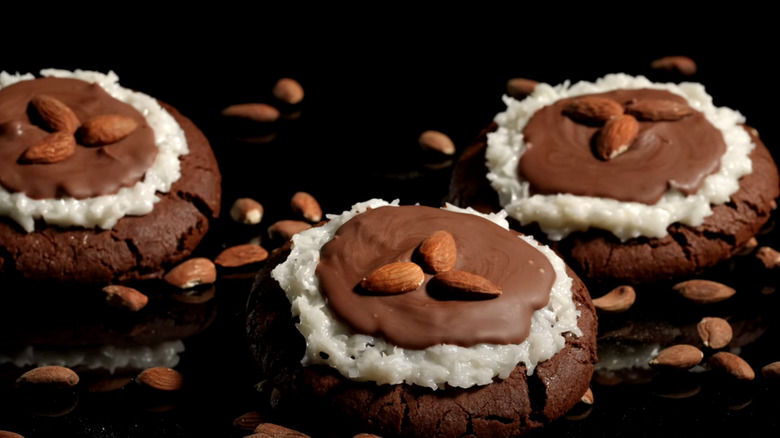 Three Almond Coconut Fudge Crumbl cookies on black background surrounded by almonds