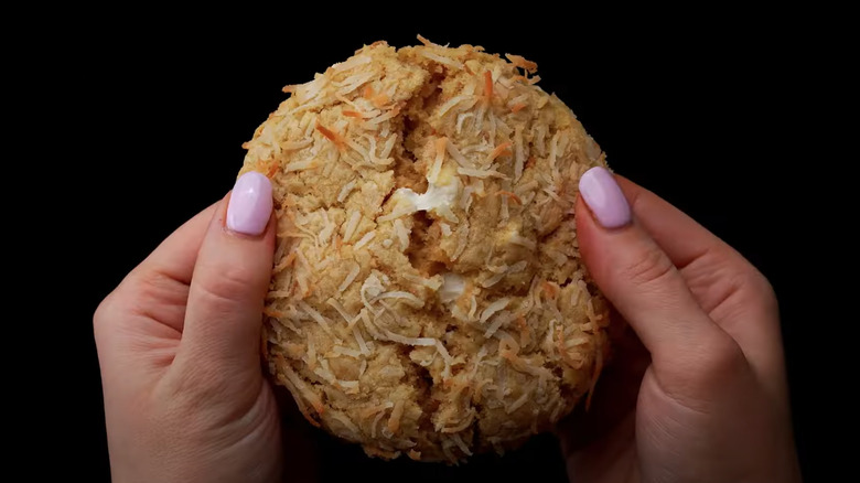 Two hands breaking a Coconut White Chip Crumbl cookie