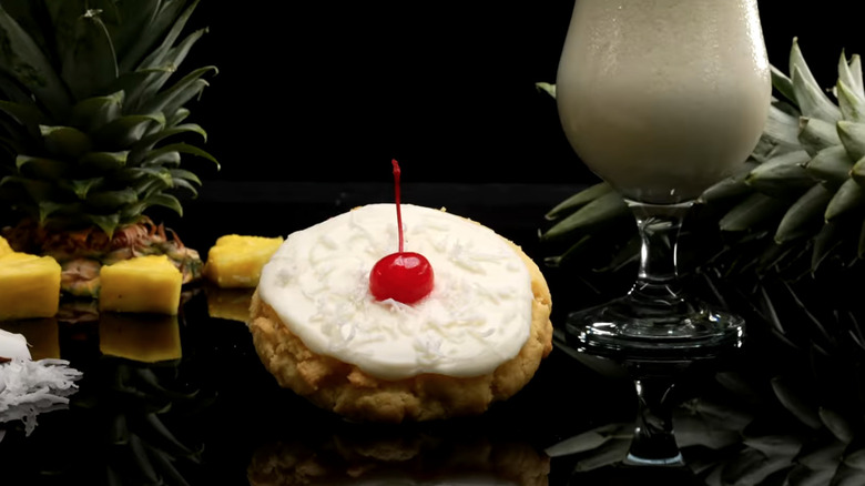 Pina Colada Crumbl Cookie in front of pineapple, coconut, and glass