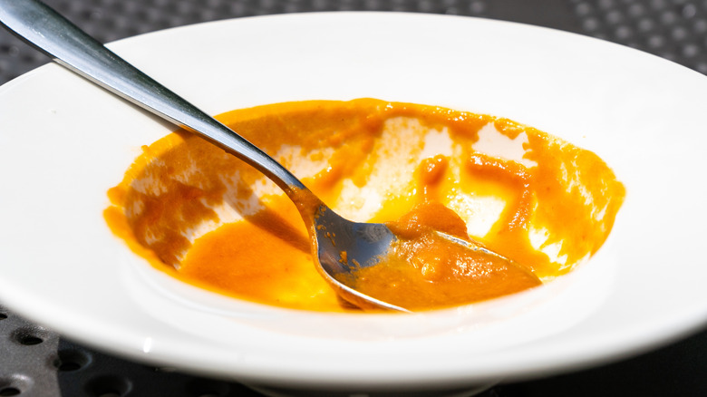 a close-up of an empty white bowl of tomato soup, with a silver spoon