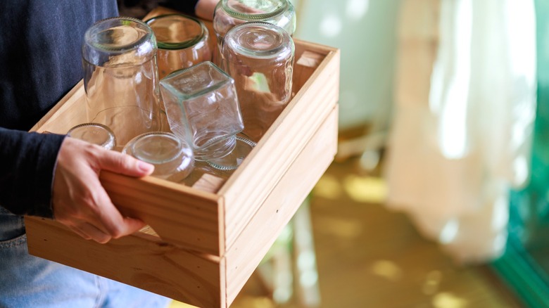 hands hold a wooden crate of empty jars