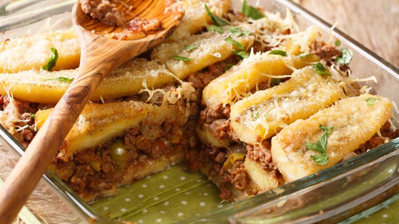 A pan of pastelón is dished up with wooden spoon
