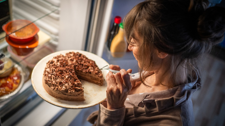 A woman eats a cake that is in the refrigerator