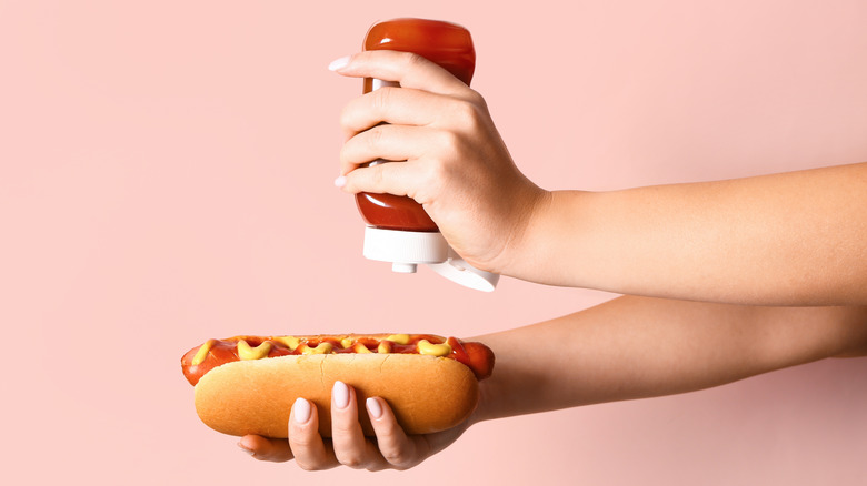 manicured hand squeezes ketchup on hot dog