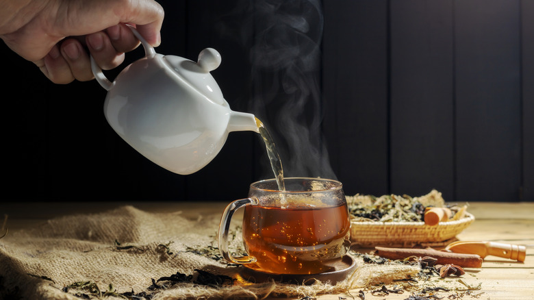 Someone pouring hot herbal tea into a glass mug