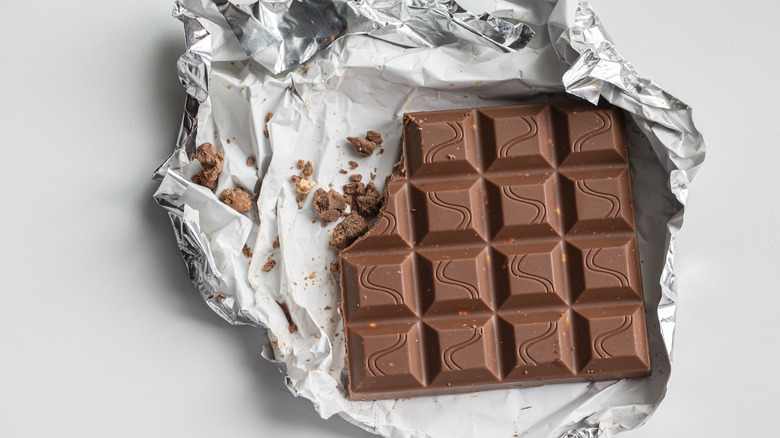 A close-up of a bar of milk chocolate in foil on a white background