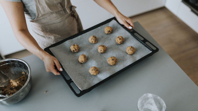 hands hold cookie sheet with raw cookies