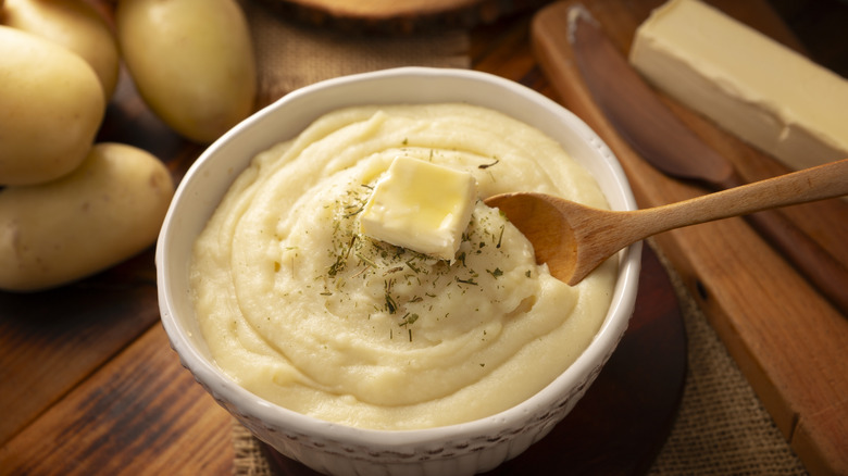 Bowl of mashed potatoes with butter, surrounded by ingredients.