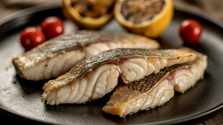 Pan seared striped sea bass on a plate with grilled lemons