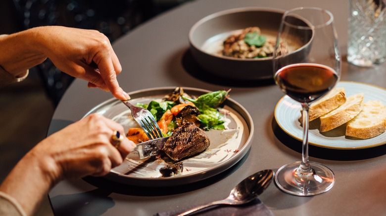 Hands cutting into steak while dining at restaurant