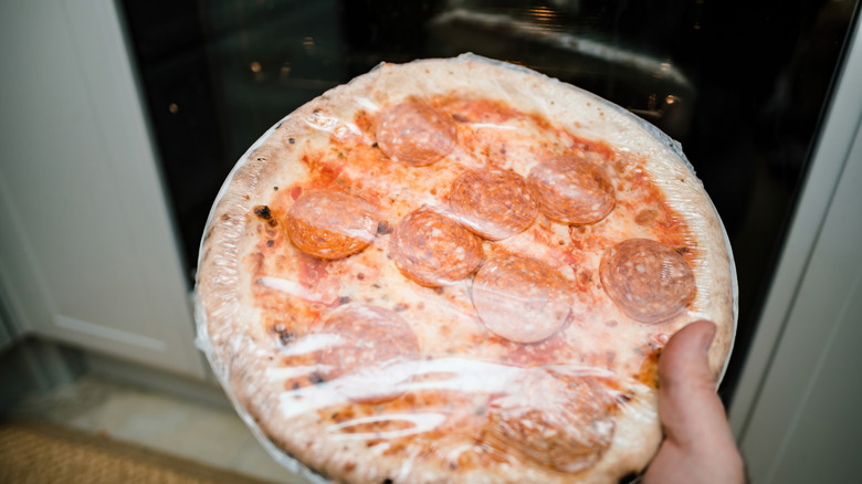 Closeup of someone holding frozen pizza still in plastic wrapping.