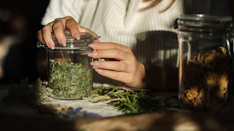 manicured hands close jar of dried herbs