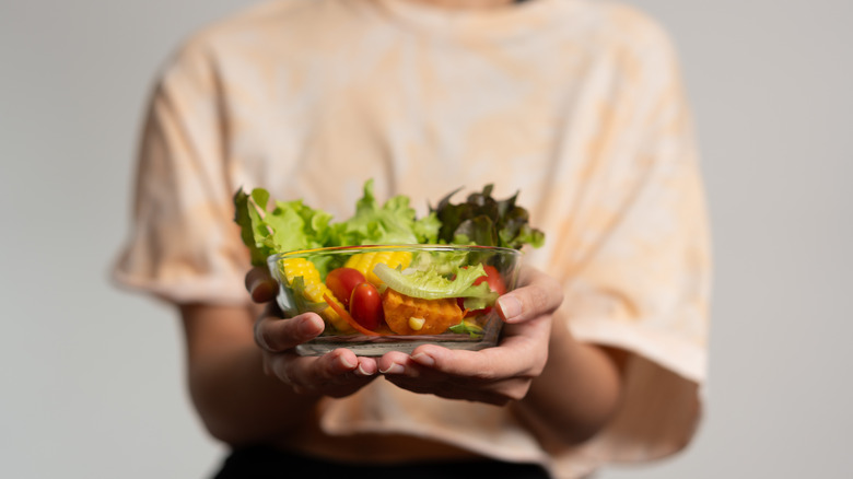 person extends salad bowl in hands