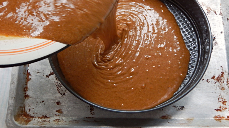 Brown cake batter being poured into a round baking pan