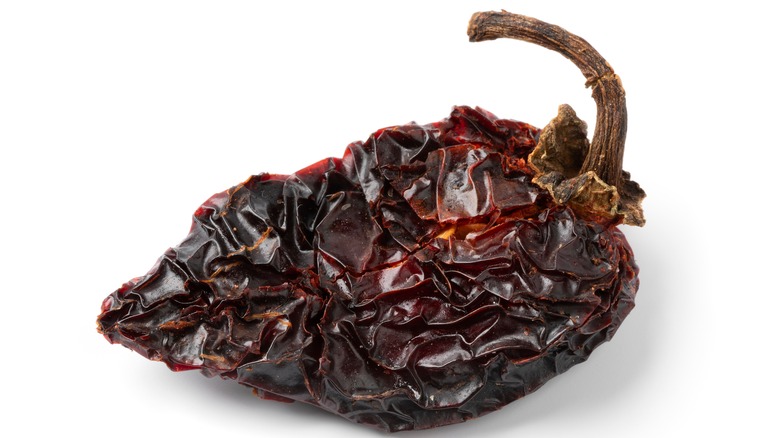 An extreme close-up of a shriveled chipotle pepper on a white background