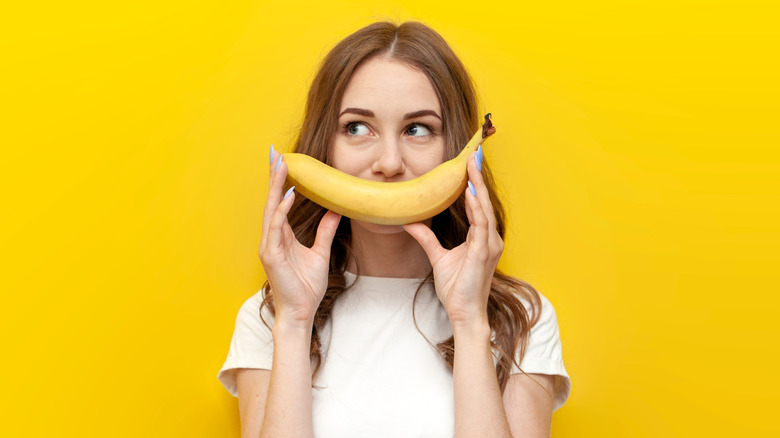 woman holds banana against yellow background