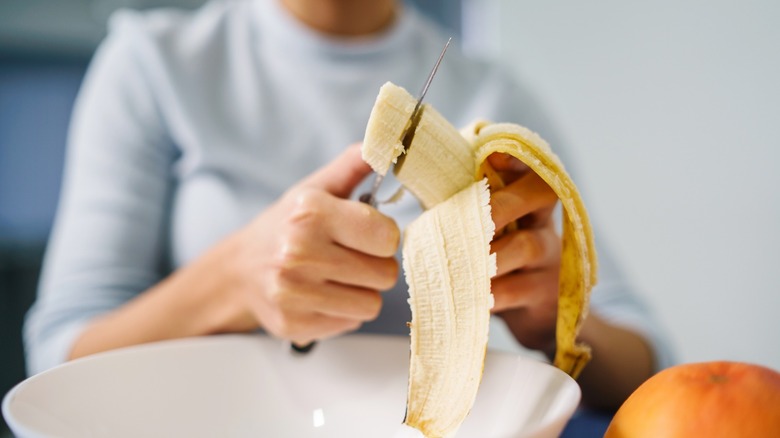 hands cutting banana into bowl