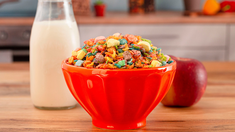 A bowl of fruity cereal with marshmallows with milk in the background.