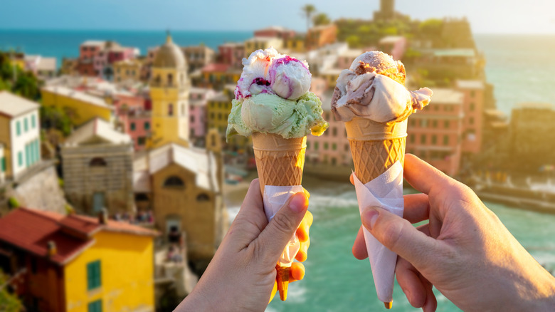 two people hold up ice cream in front of Italy's coast
