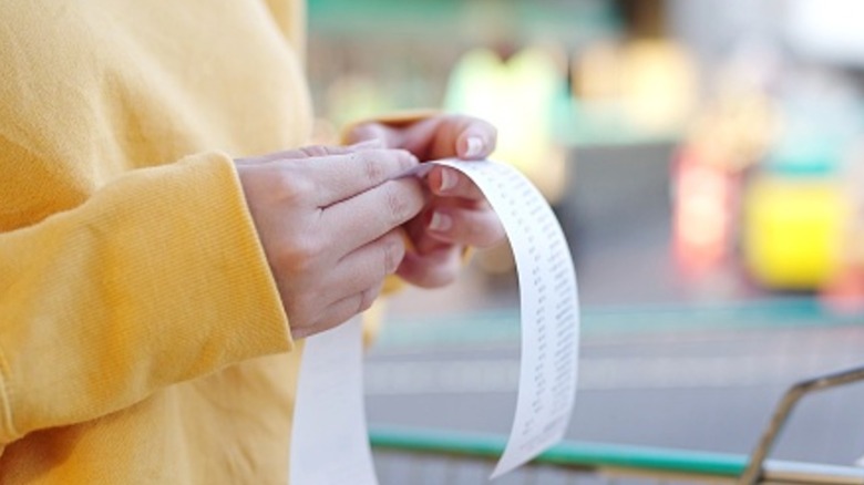 Close up of woman in a yellow sweatshirt checking a till receipt