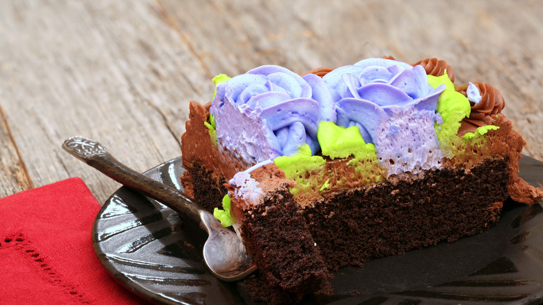 Chocolate sheet cake covered with purple and green icing on a plate with a fork