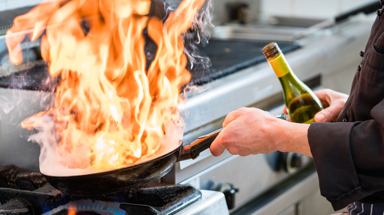 A close-up of a chef flambéing food in a pan