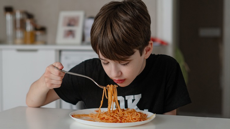 A teenage boy eating a plate of spaghetti and sauce