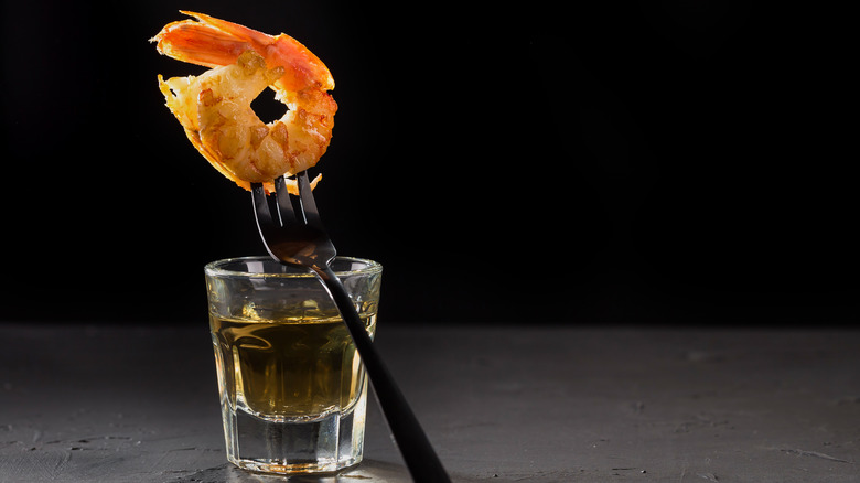 A fork skewering a shrimp, balanced on a shot of tequila