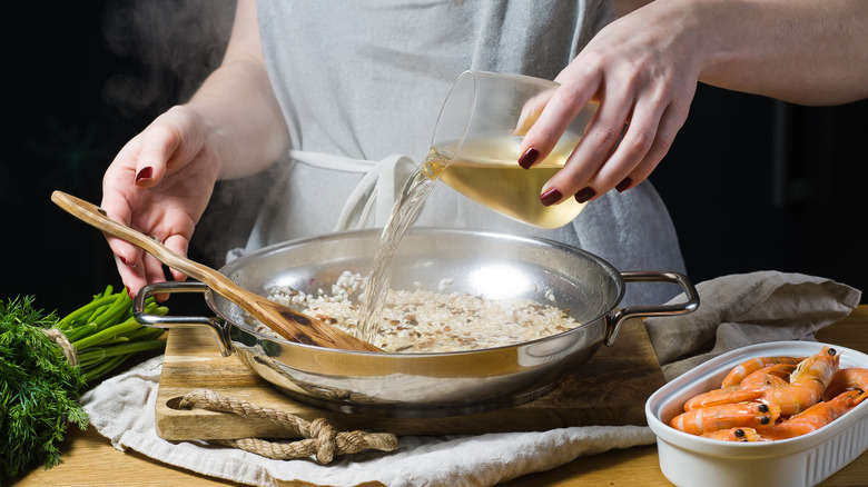A close up of a woman pouring white wine into a cooking pan