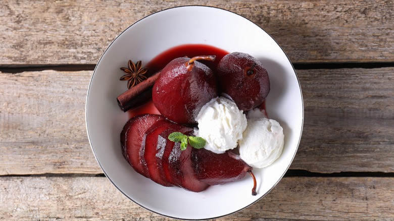 A bowl of red wine-poached pears and ice cream, in a white bowl on a wooden table