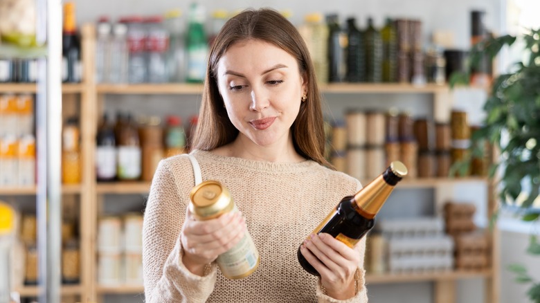 Woman deciding between a can or bottle of beer