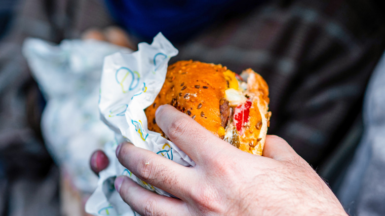 Hands holding burger in wrapper, close-up.